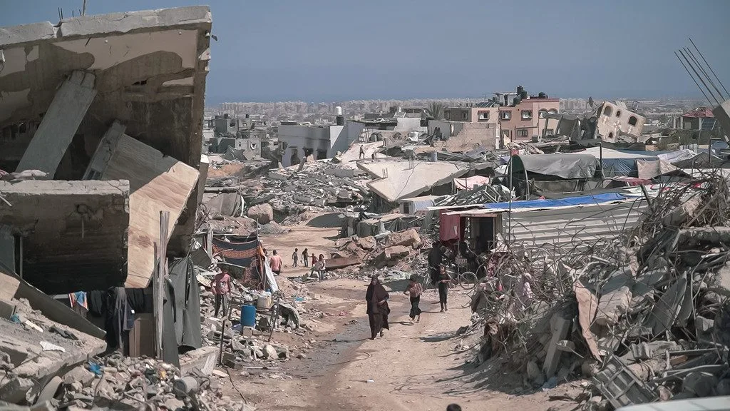 Photo Source: Image showing people walking through a heavily destroyed urban area in Gaza. Jaber Jehad Badwan, via CC portal.