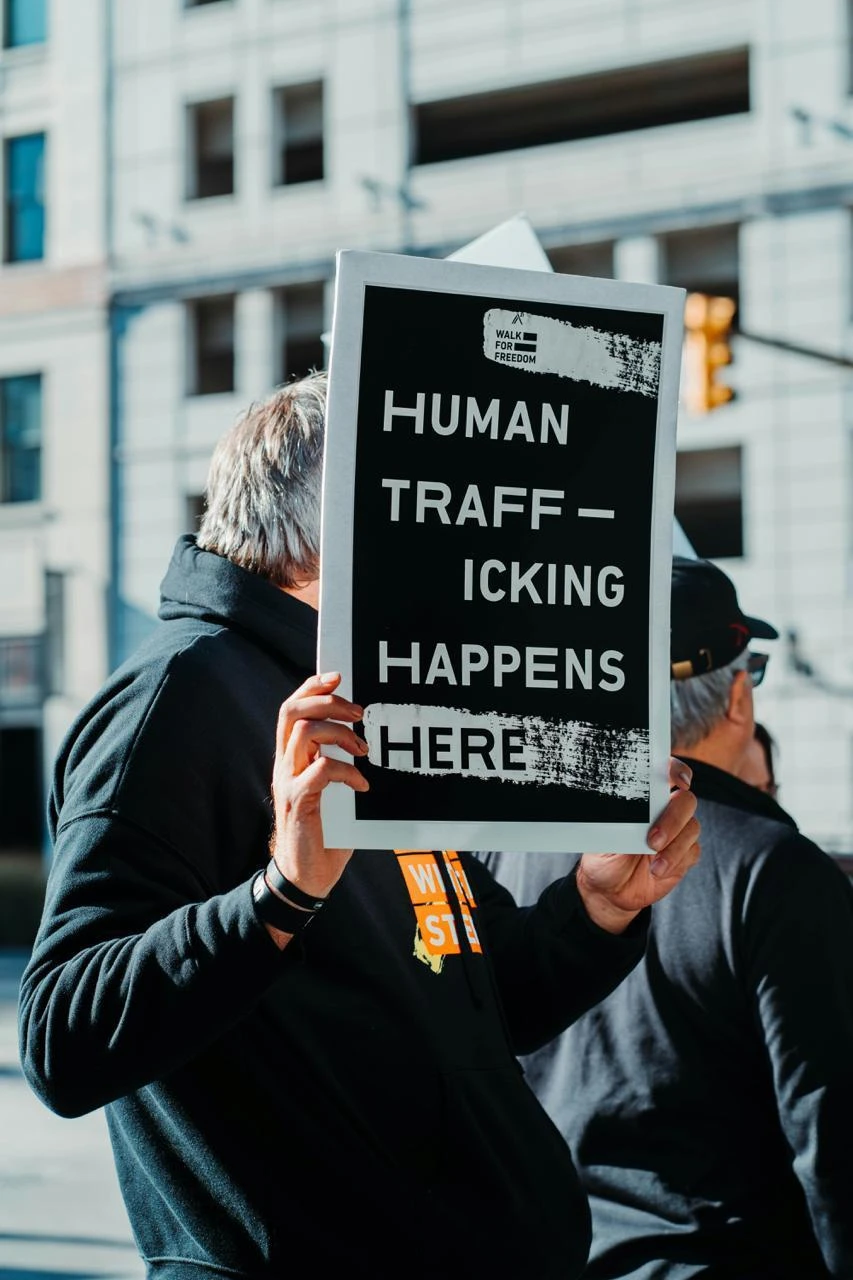 Man in black jacket holding a black and white quote board reading Human Trafficking Happens Here.